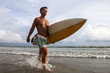 Photo: Strong man holding surf board and walking along beach Strong man holding surf board and walking along beach