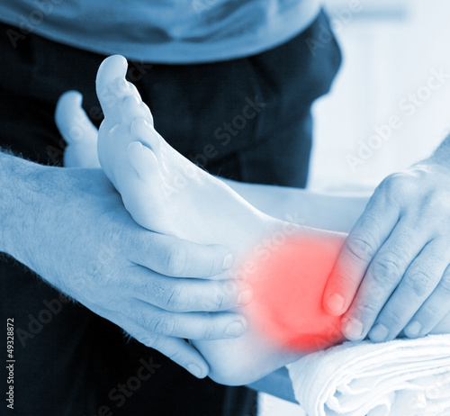 Photo: Physiotherapist touching patients highlighted ankle Physiotherapist touching patients highlighted ankle
