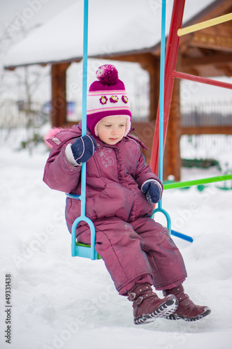 Photo: Adorable girl swings on winter snowed playground Adorable girl swings on winter snowed playground