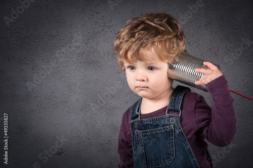Photo: Young kid listen to tin can telephone over grunge background. Young kid listen to tin can telephone over grunge background.