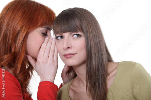 Photo: Woman whispering into her friend's ear Woman whispering into her friend's ear