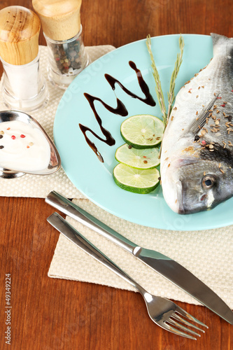 Photo: Fish dorado with lemon on plate on wooden table close-up Fish dorado with lemon on plate on wooden table close-up