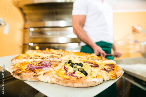 Photo: Man pushing the finished pizza from the oven Man pushing the finished pizza from the oven