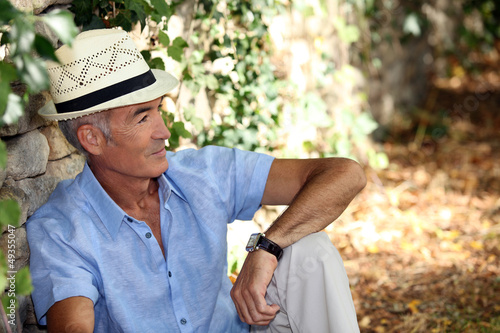 Photo: Elderly man sitting against the stone wall Elderly man sitting against the stone wall