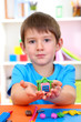 Cute little boy holding hand-made plasticine hourse over desk