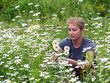 beautiful young woman sitting on a flowering meadow with daisies