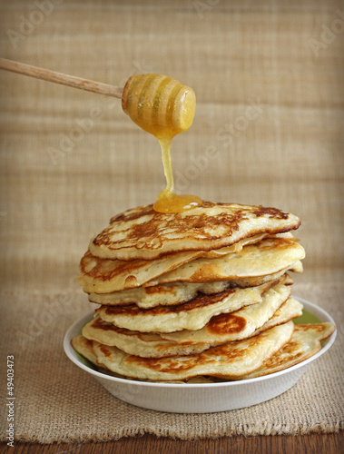 Photo: tasty pancakes with honey and wooden dipper on canvas background tasty pancakes with honey and wooden dipper on canvas background