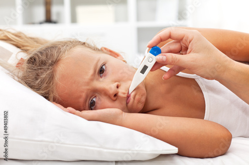 Photo: Sick little girl with thermometer laying in bed Sick little girl with thermometer laying in bed