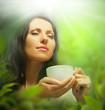 Photo: Woman with tea cup on background of blurred green leaves Woman with tea cup on background of blurred green leaves