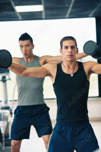 Photo: Two young men exercising with dumbbells in the gym. Two young men exercising with dumbbells in the gym.