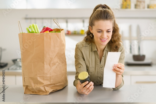 Photo: Smiling young housewife examines purchases and check after shopp Smiling young housewife examines purchases and check after shopp