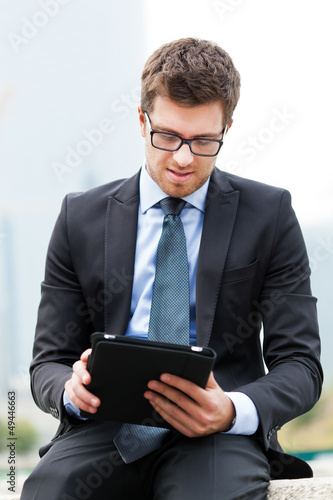 Photo: Businessman sitting on a bench and using a tablet Businessman sitting on a bench and using a tablet