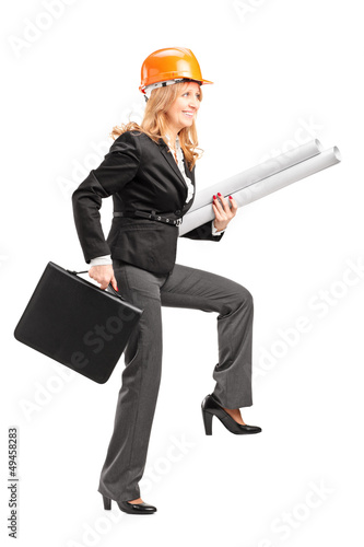 Photo: Mature female architect with helmet holding blueprints and suitc Mature female architect with helmet holding blueprints and suitc
