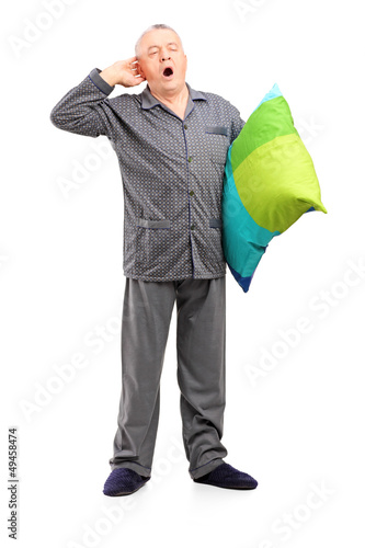 Photo: Full length portrait of a sleepy mature man in pajamas holding a Full length portrait of a sleepy mature man in pajamas holding a