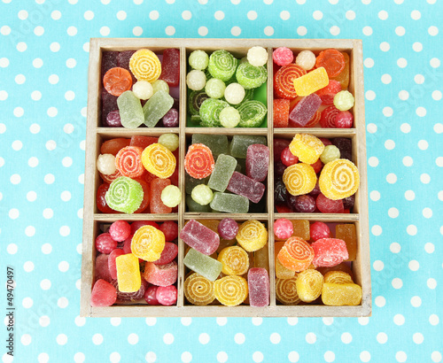 Photo: Multicolor candies in wooden box, on color background Multicolor candies in wooden box, on color background