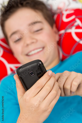 Photo: Junge liegt entspannt mit Handy / Smartphone im Bett Junge liegt entspannt mit Handy / Smartphone im Bett