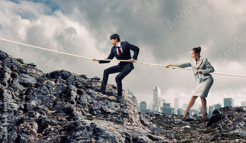 Photo: Two businessmen pulling rope atop of mountain Two businessmen pulling rope atop of mountain
