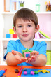 Cute little boy holding hand-made plasticine hourse over desk