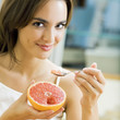 Portarit of young woman eating grapefruit at home