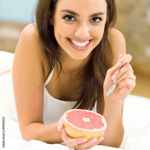 Photo: Portarit of young woman eating grapefruit at home Portarit of young woman eating grapefruit at home