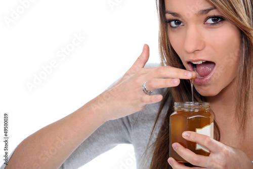Photo: Brunette dipping finger in honey jar Brunette dipping finger in honey jar