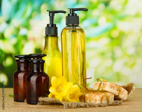Photo: Liquid and hand-made soaps on wooden table, on green background Liquid and hand-made soaps on wooden table, on green background