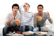 male trio watching soccer match on TV and eating hamburgers