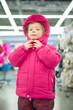 Photo: Adorable girl fitting winter jacket and hat in sport store Adorable girl fitting winter jacket and hat in sport store