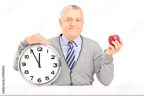 Photo: Smiling gentleman sitting and holding a wall clock and an apple Smiling gentleman sitting and holding a wall clock and an apple