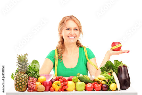 Photo: Smiling woman with fruits and vegetables holding an apple with m Smiling woman with fruits and vegetables holding an apple with m