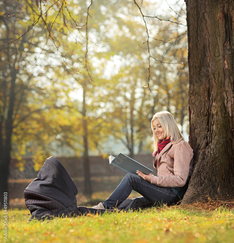 Photo: Young mother sitting in a park with her baby in a carrycot and r Young mother sitting in a park with her baby in a carrycot and r