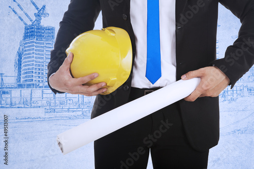 Photo: Businessman holds safety helmet and blueprint Businessman holds safety helmet and blueprint