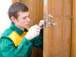Young handyman in uniform changing door lock