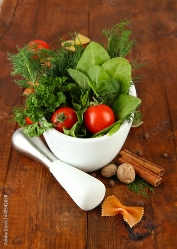 Photo: Herbs and spices in ceramic mortar, on wooden background Herbs and spices in ceramic mortar, on wooden background