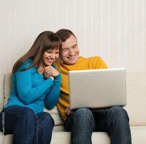 Photo: Happy couple sitting on sofa with laptop Happy couple sitting on sofa with laptop