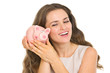 Happy young woman shaking piggy bank