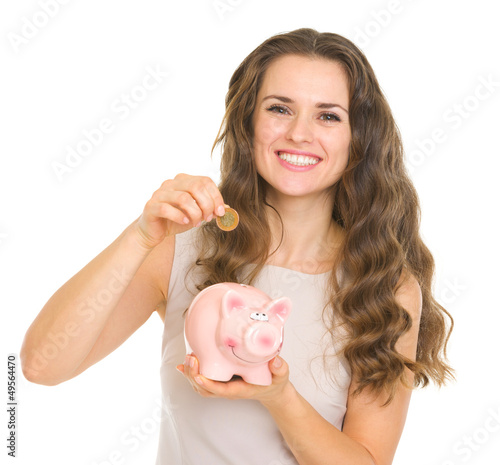 Photo: Happy young woman putting coin into piggy bank Happy young woman putting coin into piggy bank