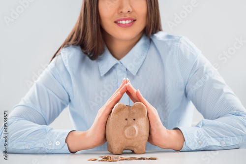 Photo: Happy business woman covering piggy bank with two hands - safety Happy business woman covering piggy bank with two hands - safety