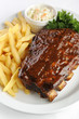 Grilled juicy barbecue pork ribs in a white plate with fries.