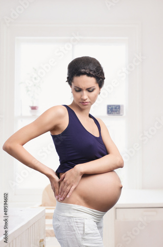 Photo: Pregnant woman standing with back pain at home Pregnant woman standing with back pain at home