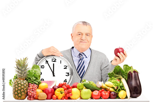 Photo: Mature man with red apple, clock and fruit and vegetables on a t Mature man with red apple, clock and fruit and vegetables on a t