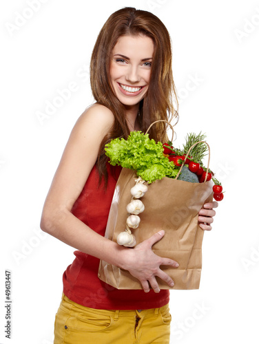Photo: Young woman holding a grocery bag full of fresh and healthy food Young woman holding a grocery bag full of fresh and healthy food