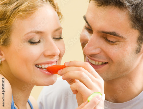 Photo: Cheerful young couple eating together tomatoes Cheerful young couple eating together tomatoes
