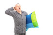 A sleepy mature man in pajamas holding a pillow and yawning