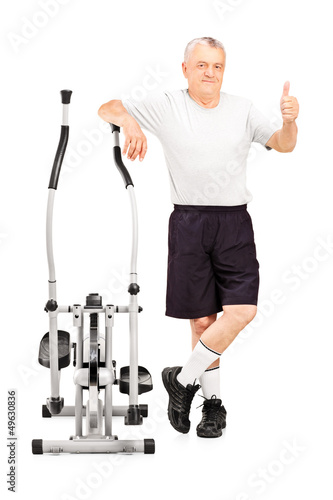 Photo: Smiling mature athlete next to a cross trainer giving thumb up Smiling mature athlete next to a cross trainer giving thumb up