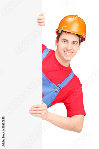 Photo: Young construction worker with helmet posing behind a panel Young construction worker with helmet posing behind a panel