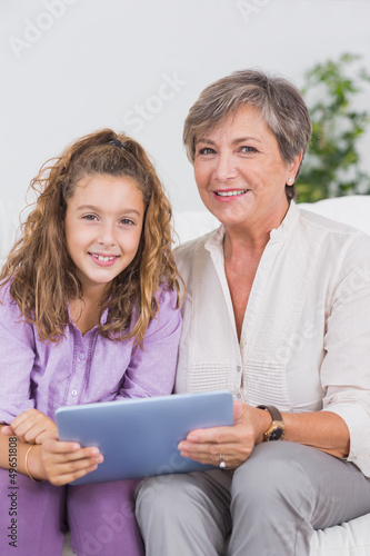 Photo: Child and her grandmother looking at the camera with tablet pc Child and her grandmother looking at the camera with tablet pc