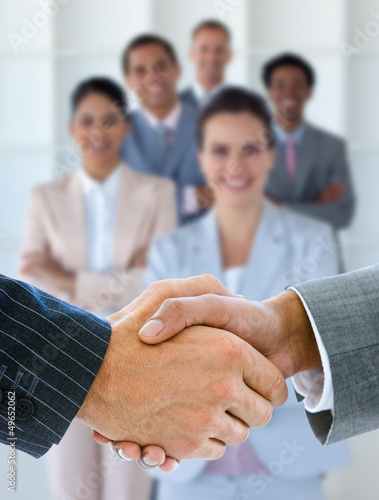 Photo: Businessmen shaking hands with team behind them Businessmen shaking hands with team behind them