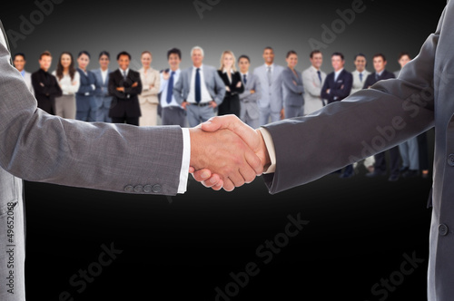 Photo: Businessmen shaking hands with large team behind them Businessmen shaking hands with large team behind them