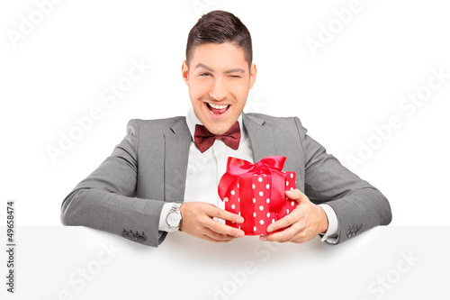 Photo: Charming young man holding a present and posing behind panel Charming young man holding a present and posing behind panel